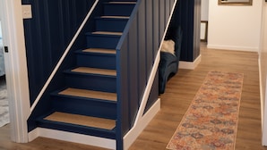A staircase with dark blue steps and white handrails, leading to a room with a patterned rug and a chair. - Secluded 5BR Retreat w/ Hot Tub, Sleeps 10 (Canfield)