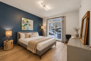 Une chambre à coucher avec un lit, une table de chevet, une lampe, une fenêtre donnant sur des rochers enneigés et un miroir.