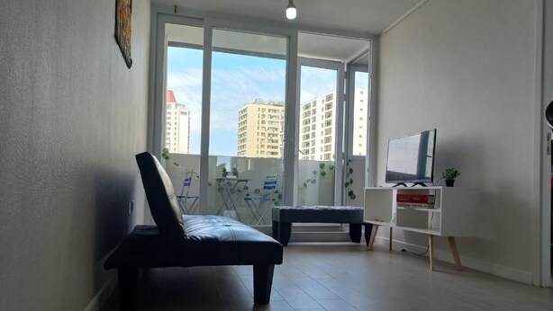Un salon moderne avec un canapé, un meuble pour la télévision et un balcon offrant une vue sur les immebles.