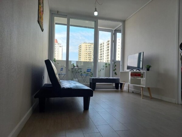 A modern living room with a sofa, a TV stand, and a balcony with a view of buildings.