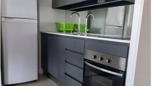 Une cuisine de taille réduite, équipée d’un réfrigérateur, d’un évier et d’un four.