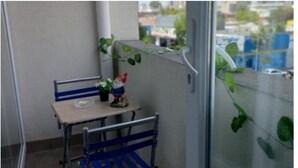 Un petit balcon avec une chaise en métal, une table et un pot de fleurs.