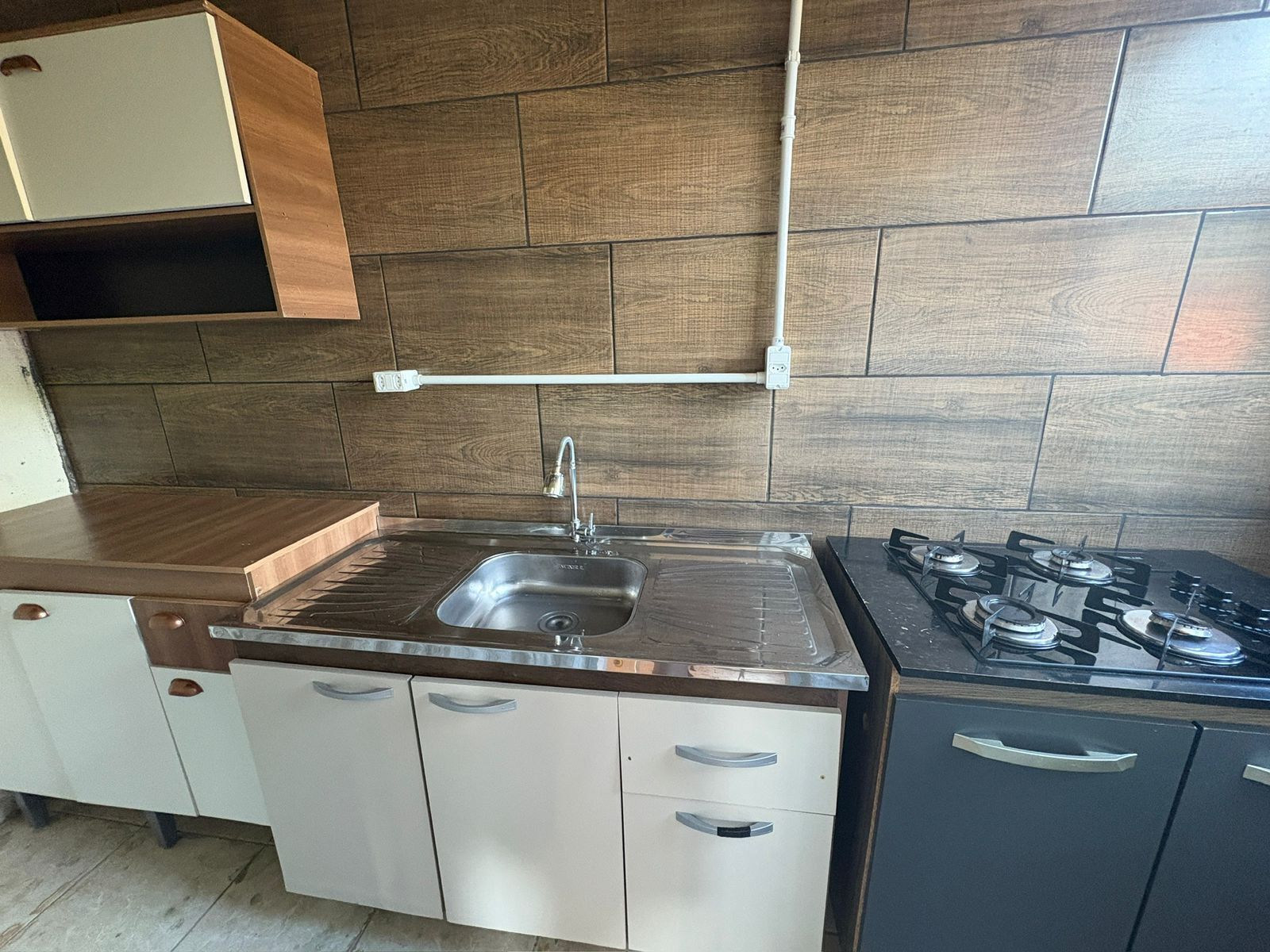 Una cocina con un lavamanos de acero inoxidable, estufa a gas, armarios blancos y encimera de madera.