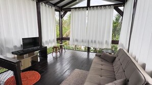 A covered outdoor seating area with a sofa, a TV, and a small table. - Pousada Charlie Brown  (Garopaba)