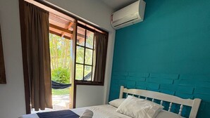 A neatly made bed with white linens, a blue headboard, and a window with curtains. - Pousada Charlie Brown  (Garopaba)