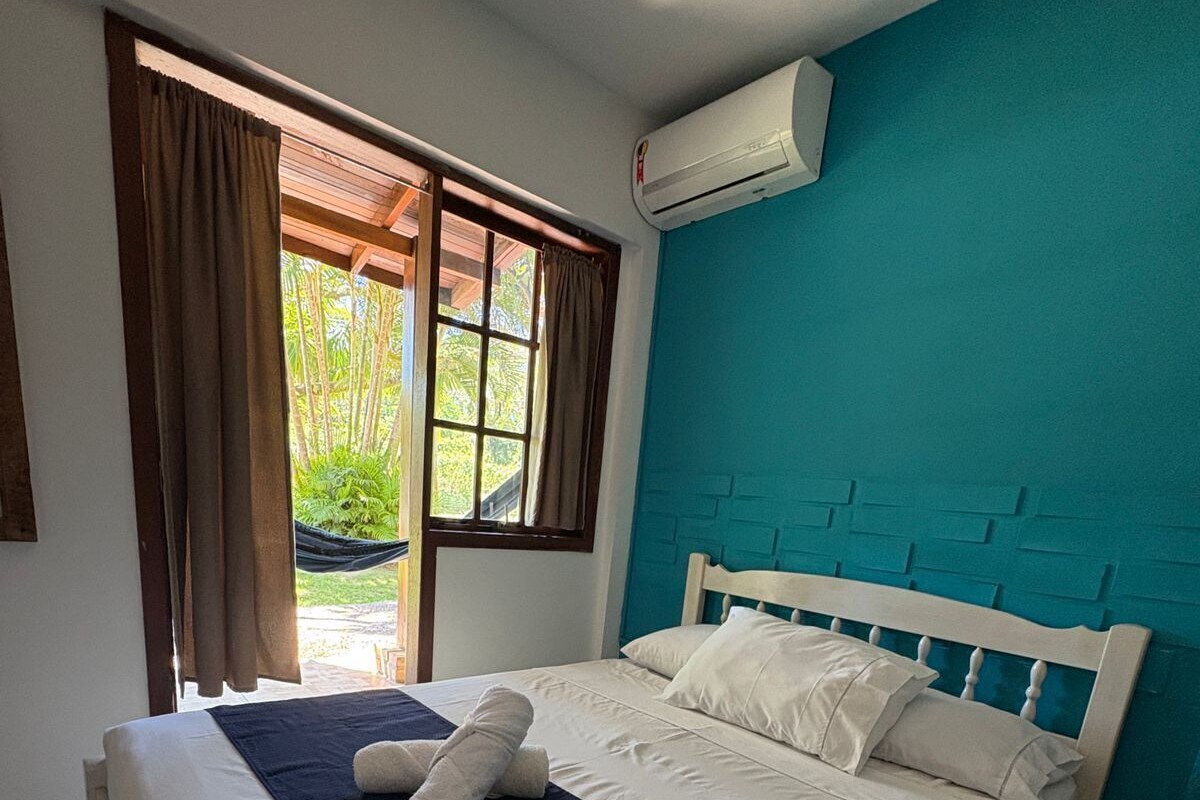 A neatly made bed with white linens, a blue headboard, and a window with curtains.