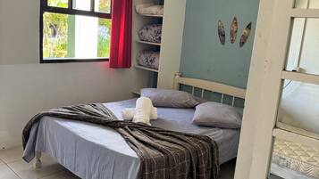 Une chambre à coucher avec un lit, une fenêtre avec des rideaux, une étagère avec des coussins et un mur décoré de différents objets.