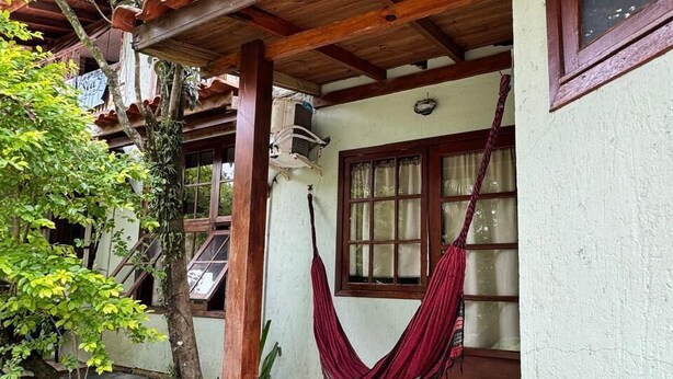 A covered outdoor area with a hammock, a window, and a brick floor. - Pousada Charlie Brown  (Garopaba)
