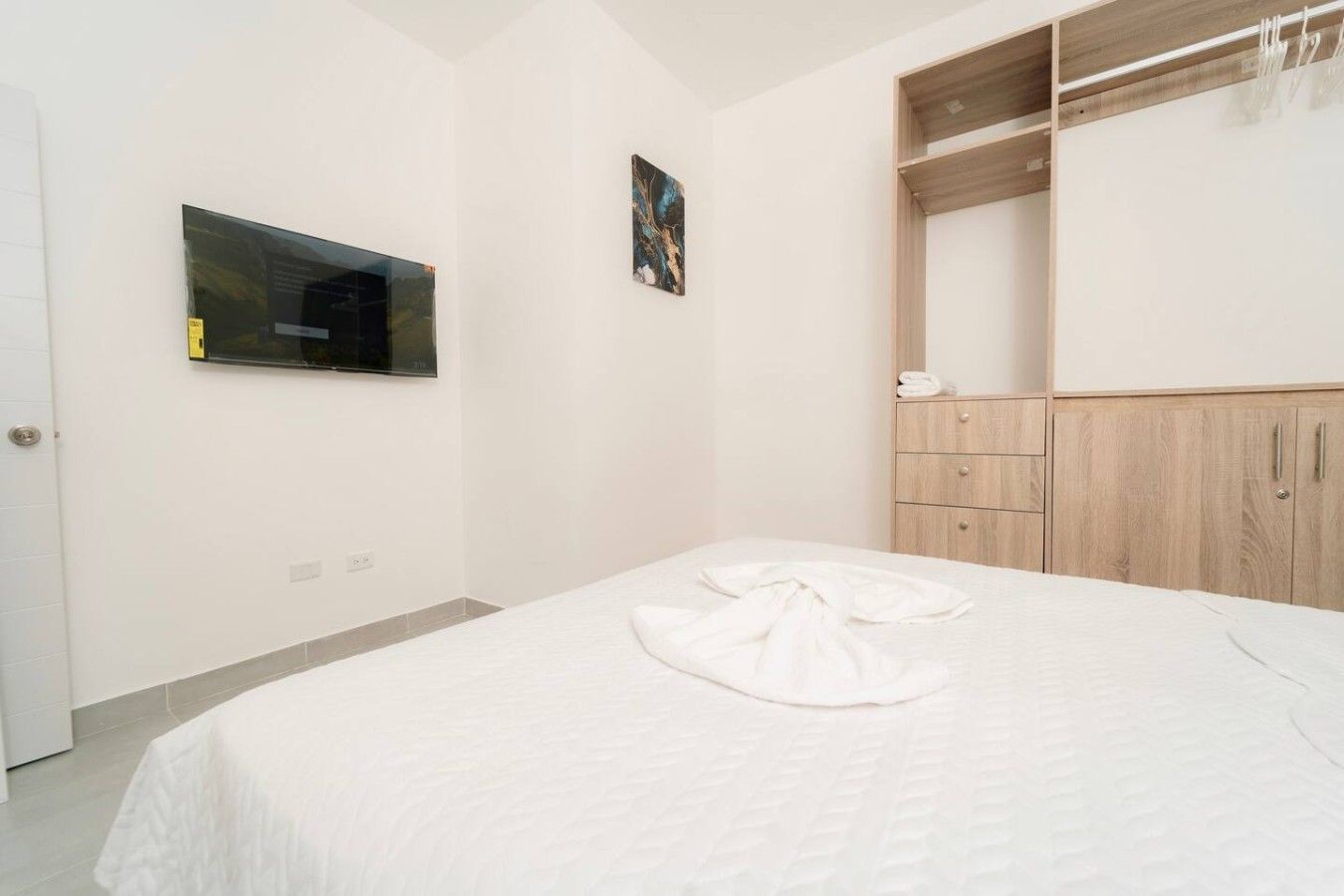 Une chambre à coucher avec un lit, une armoire, un miroir et un tableau accroché au mur.