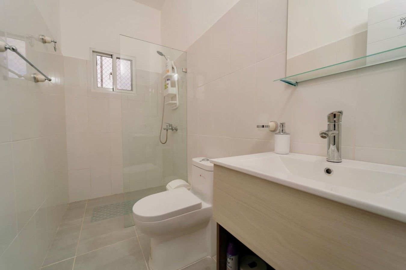 Une salle de bain avec une douche à parois de verre, des toilettes, un lavabo avec un miroir au-dessus et une fenêtre.