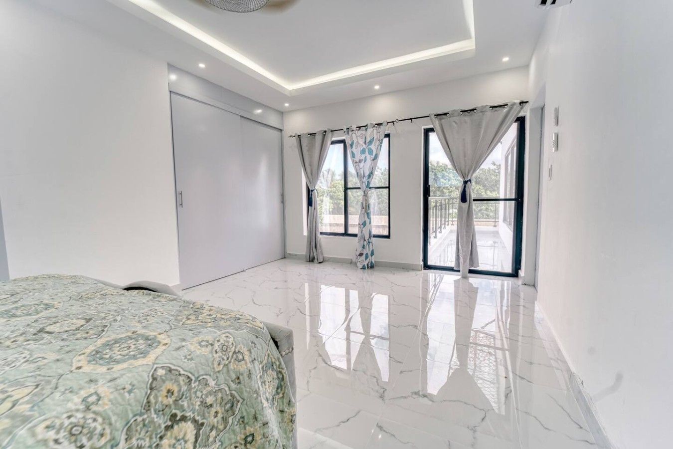Une chambre spacieuse avec un grand lit, une armoire et une vue sur l’extérieur grâce à de grandes fenêtres.