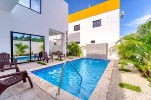 Une piscine offrant une vue dégagée sur le ciel, entourée de chaises longues et bordée d’un bâtiment moderne dont les accents de couleur sont jaune.