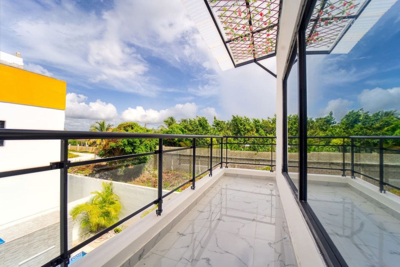 Un balcon doté d’une balustrade en verre, offrant une vue sur la verdure et un ciel dégagé.