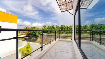 Un balcon doté d’une balustrade en verre, offrant une vue sur la verdure et un ciel dégagé.