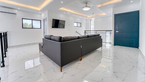 Een moderne woonkamer met een hoekbank, een flatscreen televisie en een trap naar een hoger niveau.