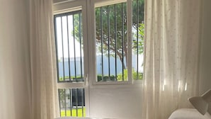 Ein Zimmer mit zwei Betten, einem Balkon und Blick auf Grünflächen und ein Gewässer.