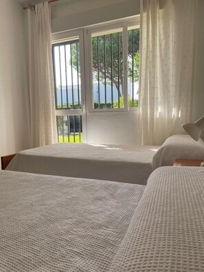 Ein Zimmer mit zwei Betten, einem Balkon und Blick auf Grünflächen und ein Gewässer.