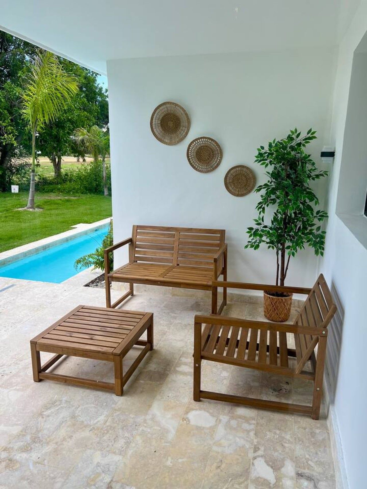 A patio area with a pool, wooden furniture, and decorative wall art.