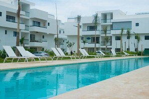 Ein Schwimmbad mit Liegestühlen und ein modernes Gebäude mit Balkonen im Hintergrund.