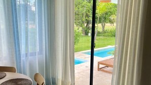 A room with a dining table, chairs, a view of a swimming pool, and a sliding glass door leading outside. - Oasis Retreat | Sleeps 4 | Free Airport Transfer (Punta Cana)