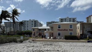 Ein Strandhotel mit der Aufschrift 'MantaRay Inn', mit Sandstrand, Palmen und modernen Gebäuden im Hintergrund.