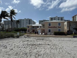 A beachfront hotel with a sign reading 'MantaRay Inn,' featuring a sandy beach, palm trees, and modern buildings in the background. - Oceanfront Suite Steps from Hollywood Beach (Hollywood)