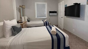 Ein Hotelzimmer mit zwei Betten, einem Deckenventilator, einem Fernseher und einem Fenster mit Jalousien.