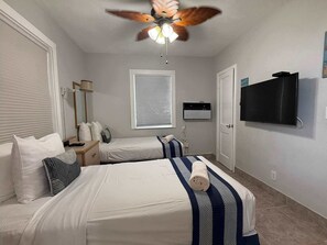 A hotel room with two beds, a ceiling fan, a TV, and a window with blinds. - Oceanfront Suite Steps from Hollywood Beach (Hollywood)