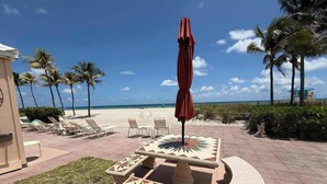 Eine Terrasse direkt am Strand mit Liegestühlen, einem gefliesten Tisch und einer Palme.
