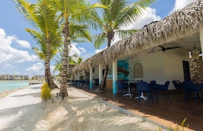 Ein Restaurant direkt am Strand mit reetgedeckten Dächern, Terrassenbestuhlung und Palmen.