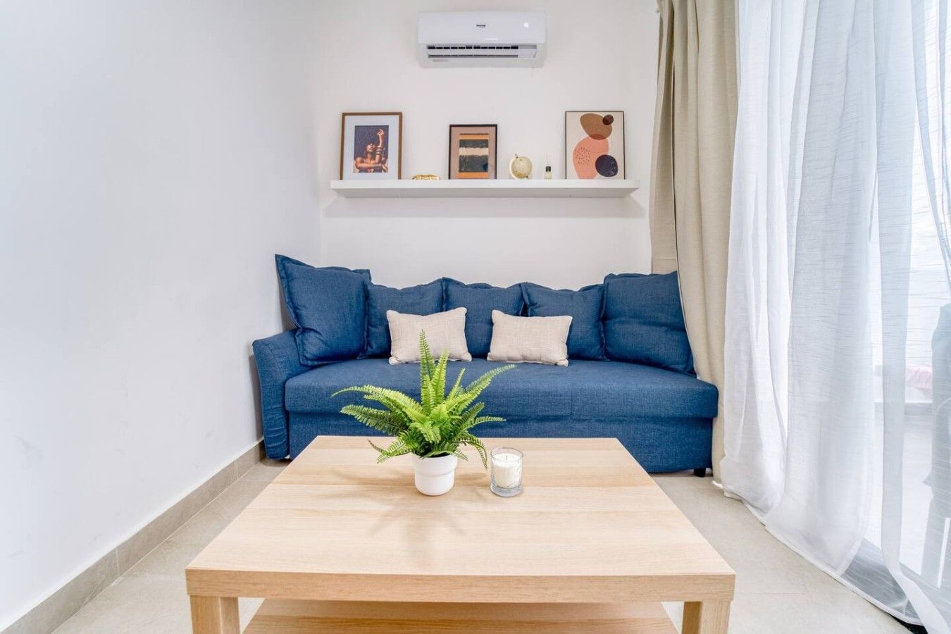 A modern living room with a blue sofa, a wooden coffee table, and a potted plant.