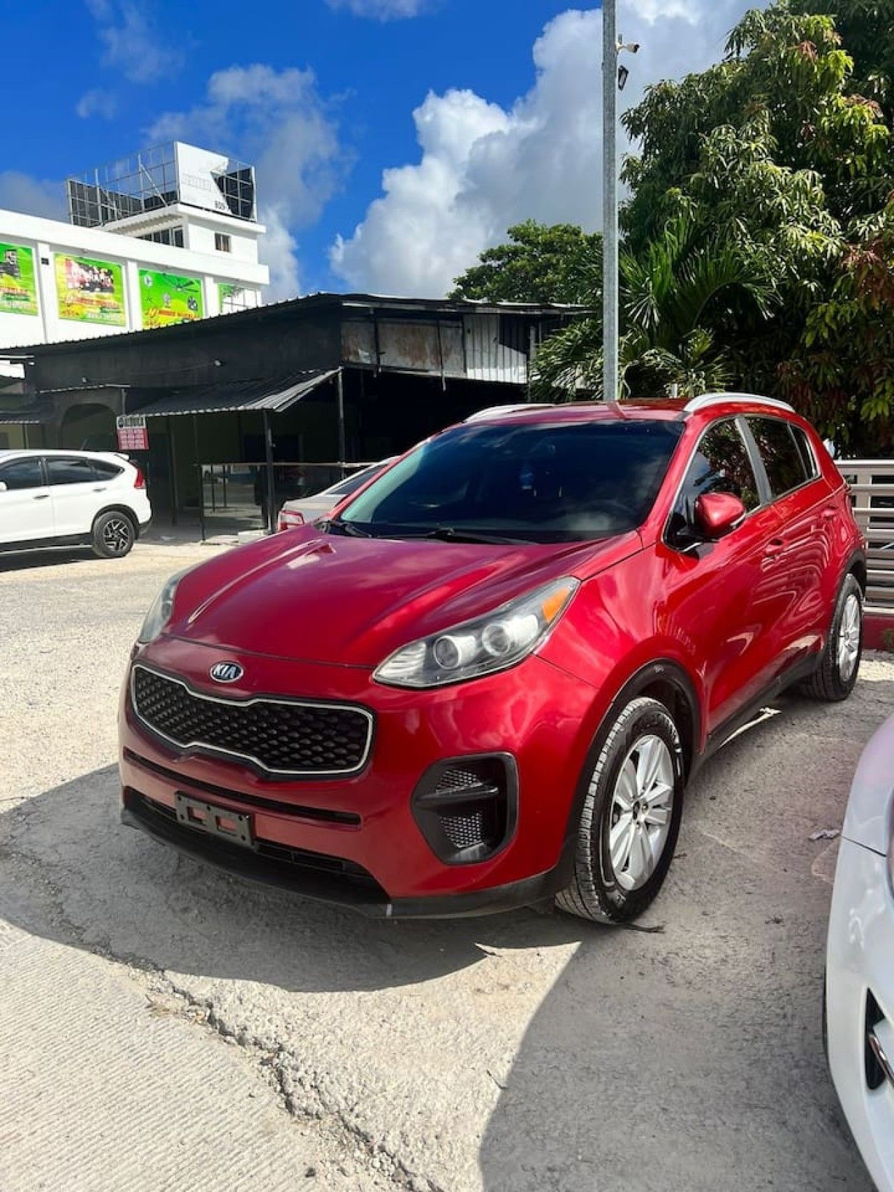 A red Kia SUV parked on a concrete surface with a building and trees in the background.
