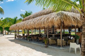 A beachside bar with thatched umbrellas, wicker furniture, and a view of palm trees. - 2-Level Retreat + Jacuzzi | FREE Electricity (Punta Cana)