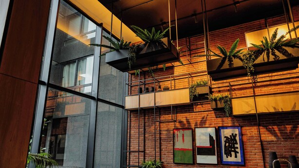 Un interior moderno con pared de ladrillo, sofá de cuero negro y plantas en macetas.