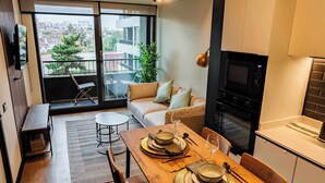 Un apartamento moderno con comedor, sofá, cocina equipada con horno y balcón con vistas a la ciudad.