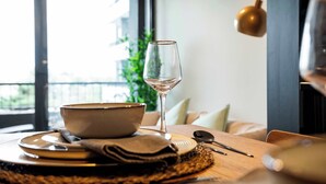 Una mesa de comedor con un bol, platos, cubiertos y una copa de vino, ubicada en una habitación con vistas a través de una ventana.