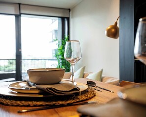 A dining table with a bowl, plates, cutlery, and a wine glass, set in a room with a view through a window. - Chic 1BR in Nunoa Cozy Balcony  Pool Access (Ñuñoa)