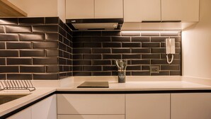 Une cuisine moderne avec un mur de briques noires derrière l’évier, une cuisinière encastrée et un téléphone fixé au mur.