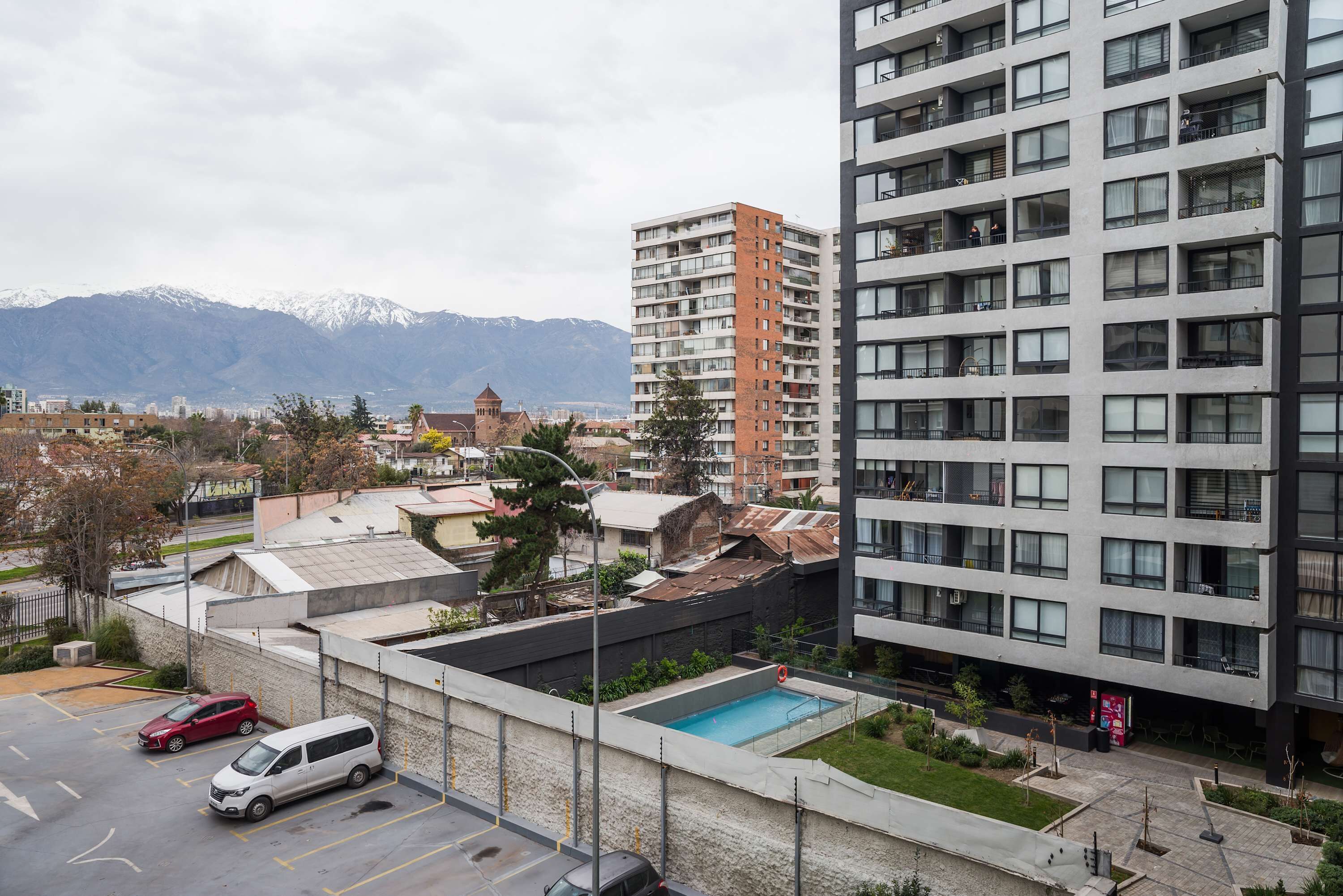 A modern building with multiple balconies, a parking area, and a view of mountains in the background.