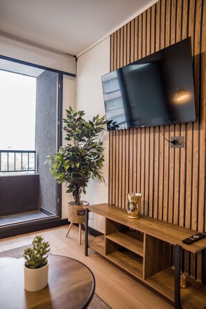 Ein modernes Wohnzimmer mit einem flachbildfernseher an einer Holzwand, einer Topfpflanze, einem runden Tisch und einer Bank.