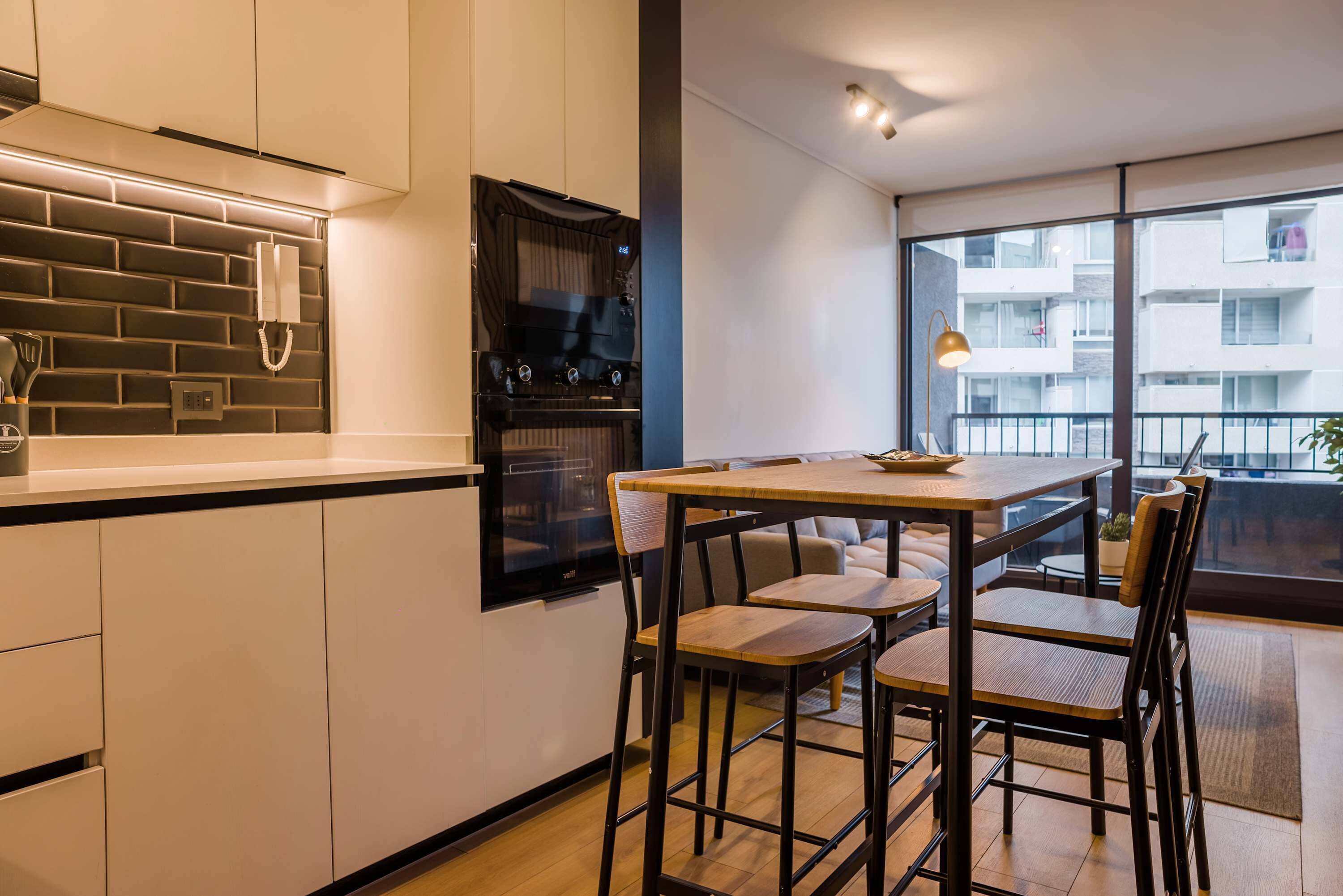 Una cocina moderna con salpicadero de ladrillo, horno empotrado y comedor con mesa y sillas.