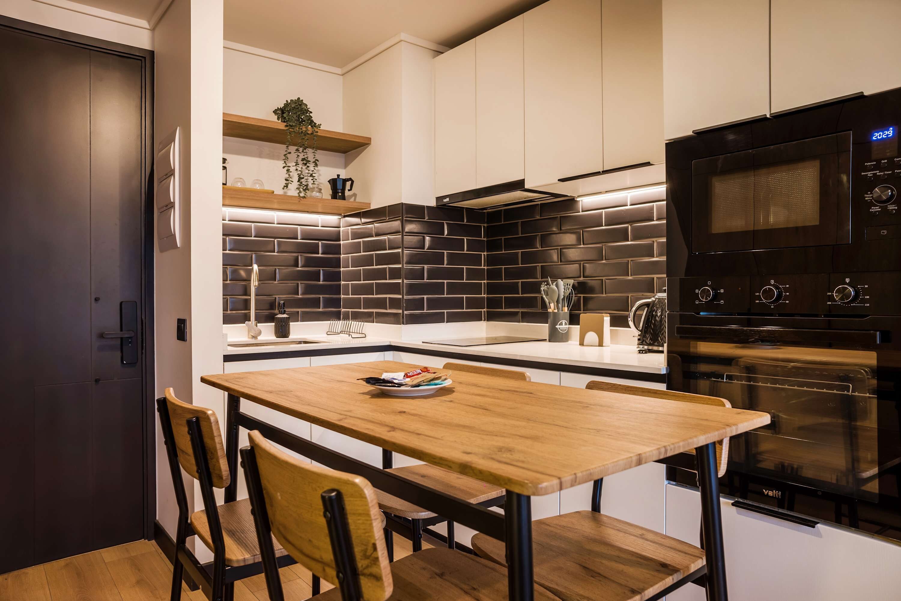 A modern kitchen with a black tiled backsplash, a wooden dining table, and a built-in oven.