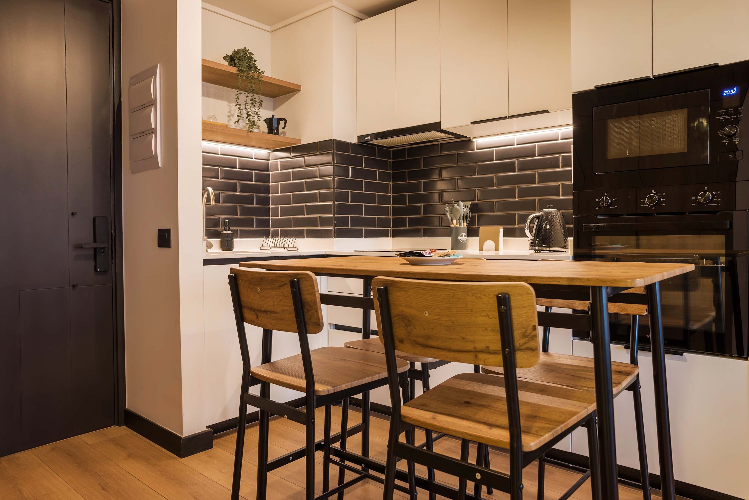 A modern kitchen with a black tiled backsplash, wooden chairs, and a built-in oven.