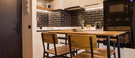 Una cocina moderna con un salpicadero de azulejos negros, sillas de madera y un horno empotrado.
