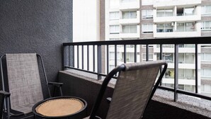 Un balcon doté d’une balustrade en métal noir, d’une chaise en osier et d’un canapé en osier.