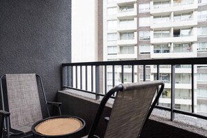 Ein Balkon mit schwarzem Metallgeländer, einem gewebten Stuhl und einer gewebten Couch.
