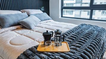 A neatly made bed with a grey blanket, a wooden tray with a coffee maker, two glasses, and a teapot.