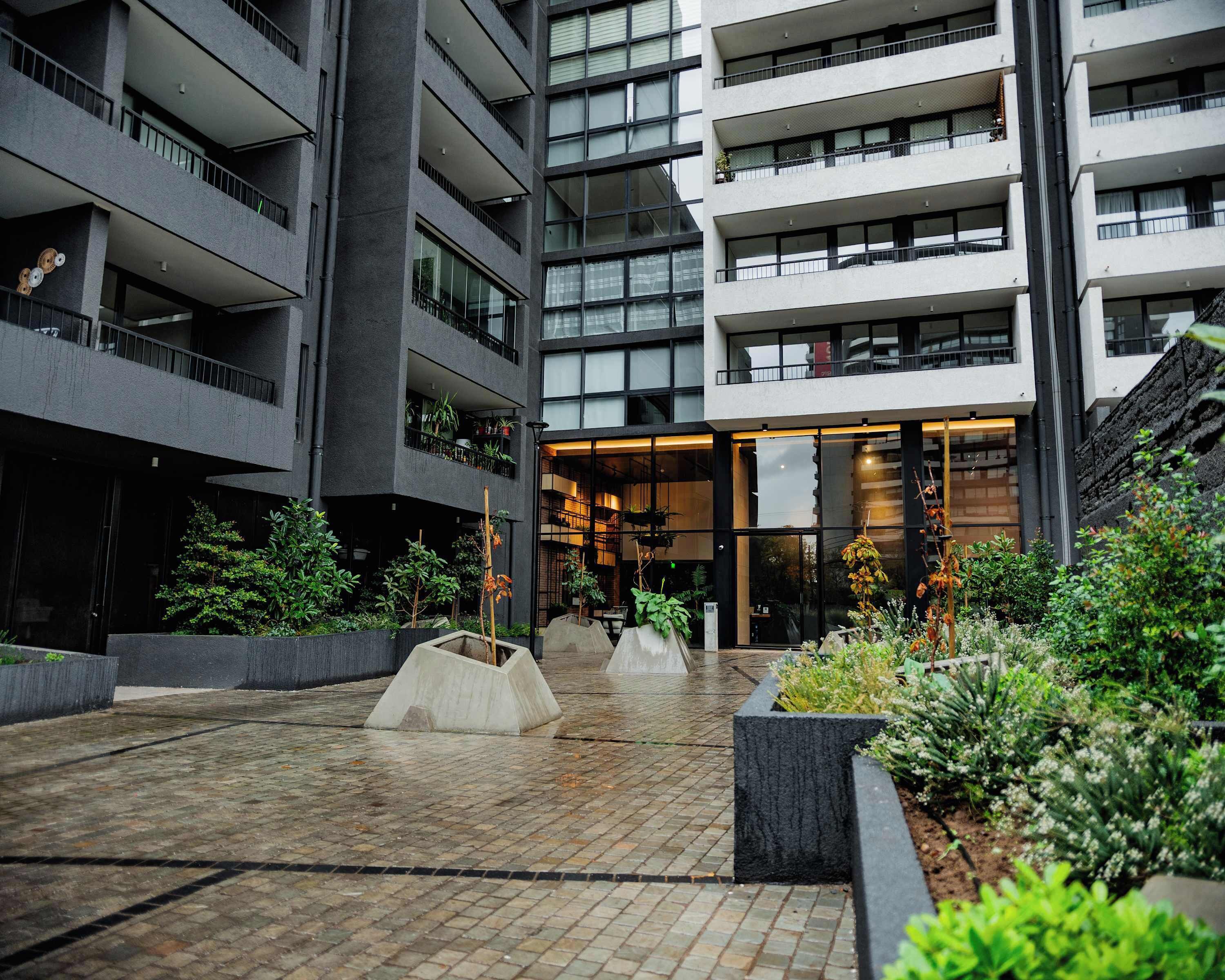 A multi-story building with balconies, a central open area with planters, and a staircase on the right.