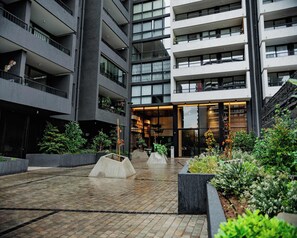 A multi-story building with balconies, a central open area with planters, and a staircase on the right.