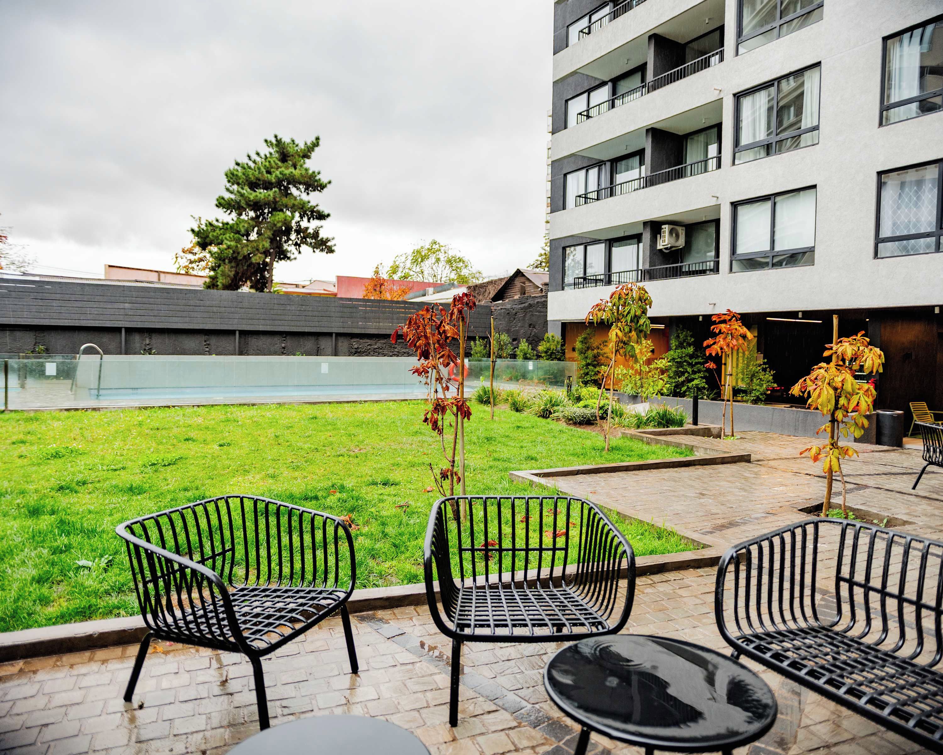 Un patio con piscina, mobiliario exterior y un edificio moderno con balcones.